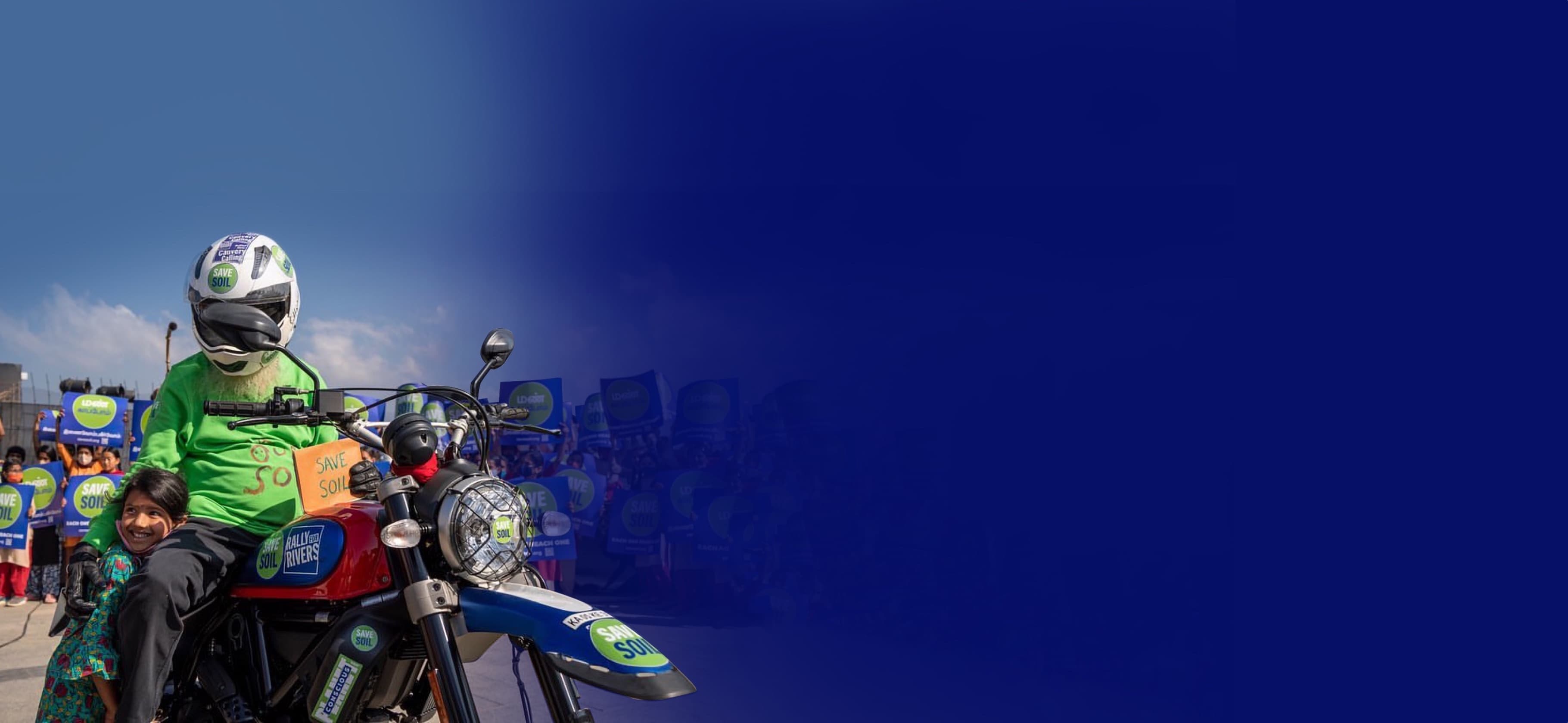 Sadhguru on motorcycle with Save Soil sign, alongside child