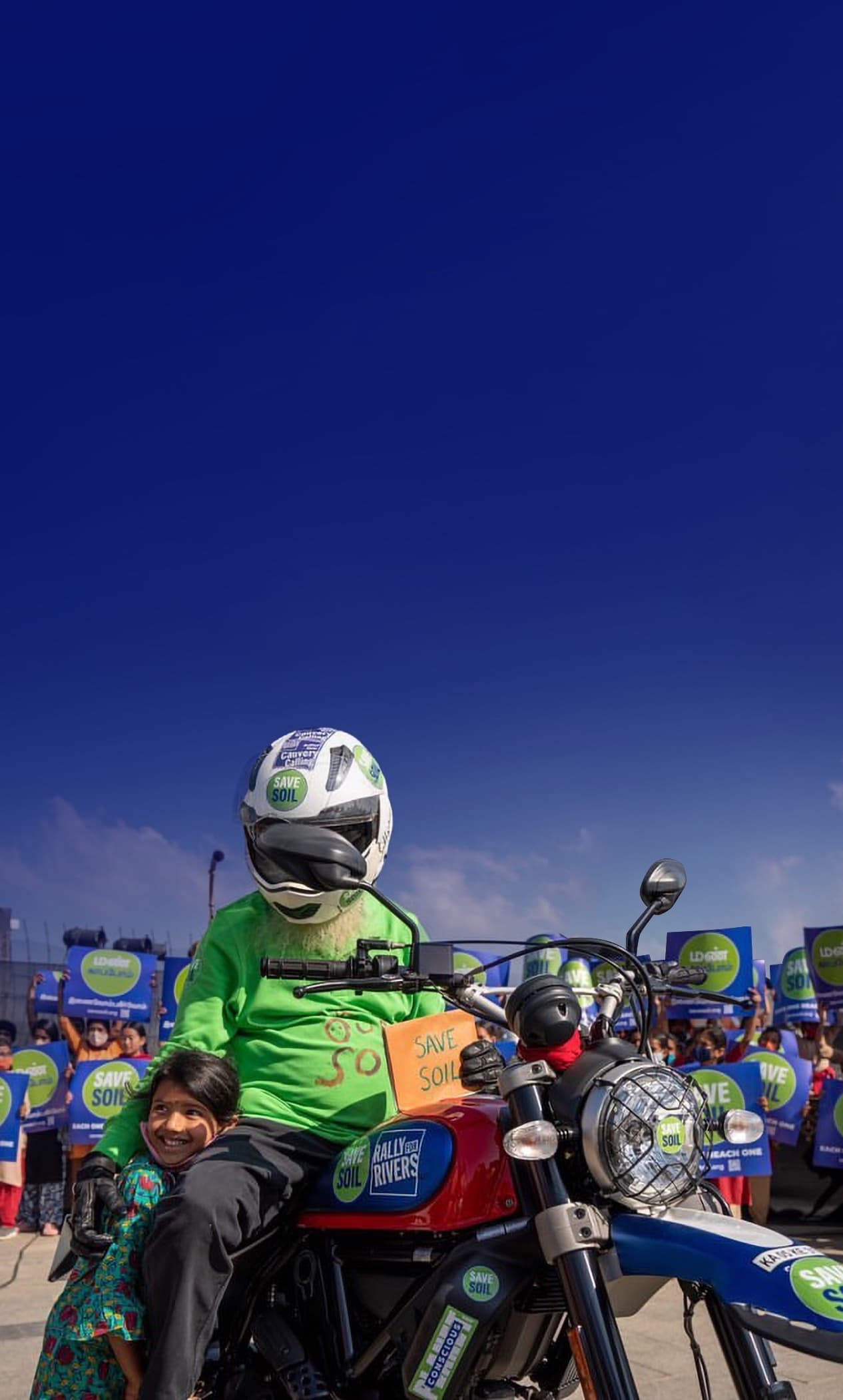 Sadhguru on motorcycle with Save Soil sign, alongside child